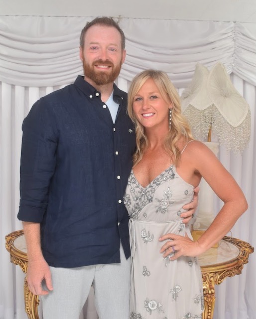 A man in a blue shirt and a woman in a cream dress posing for a photo